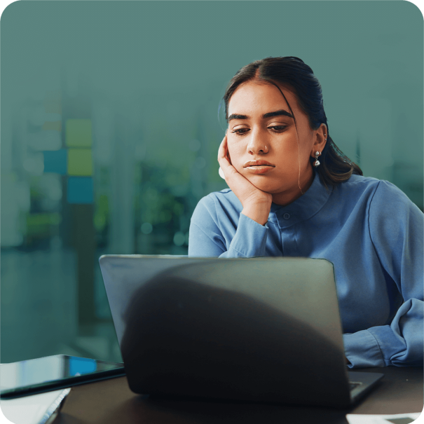A woman seated at a desk, focused on her laptop, with a notepad and pen beside her.