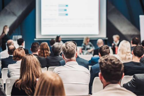 Audience seated in an auditorium attending a presentation on a large screen during a professional association conference.